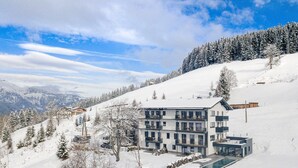 Un hôtel moderne à plusieurs étages, doté d’une piscine, entouré d’arbres et de montagnes couverts de neige.