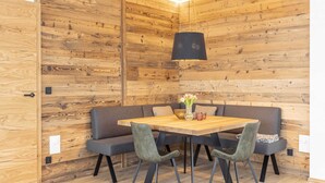 Un espace repas moderne avec un mur en bois, une table ronde et deux bancs recouverts d’un tissu gris.