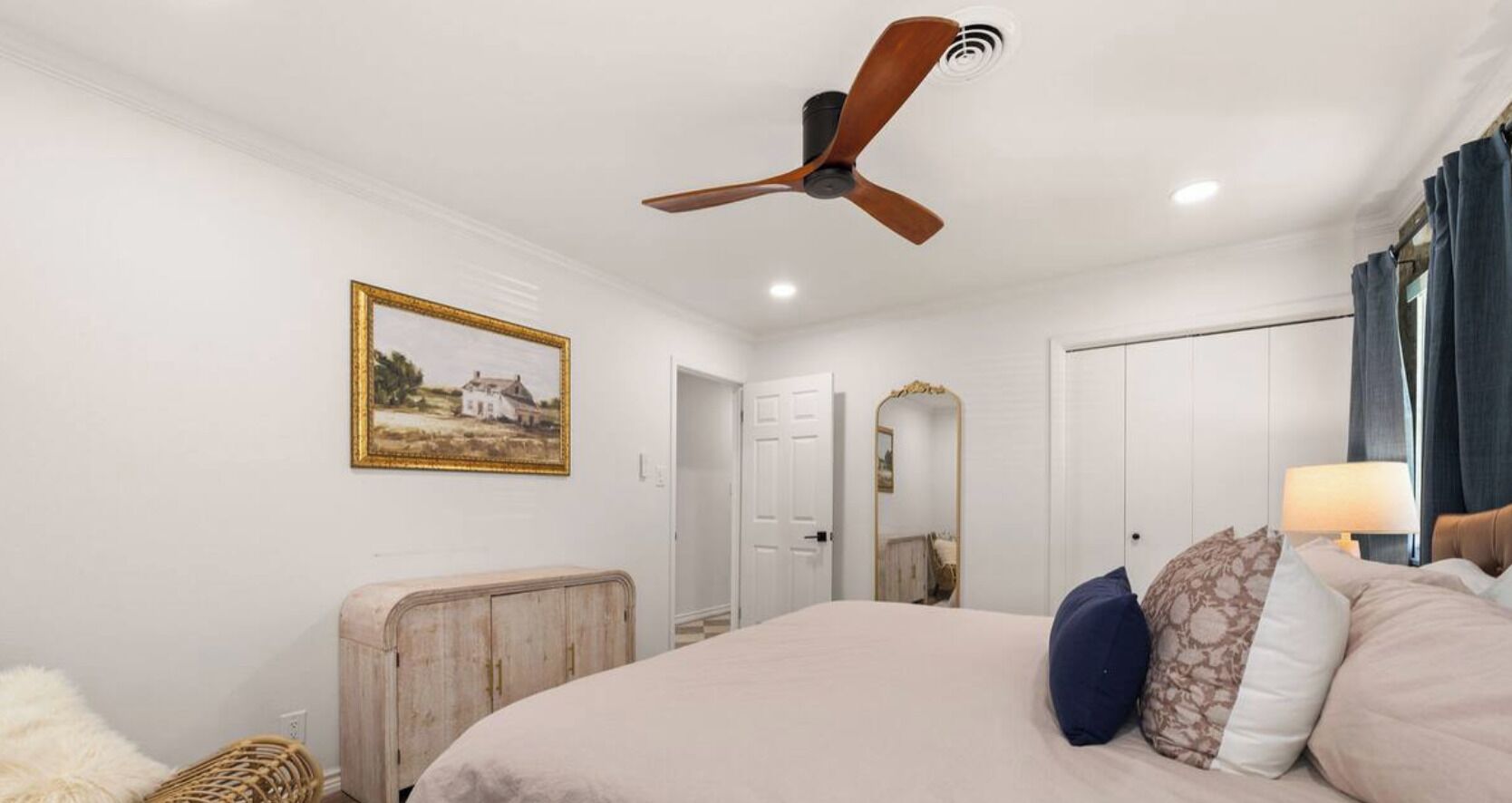 Un dormitorio con cama, ventilador de techo, un cuadro en la pared, armario y espejo.
