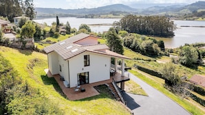 Una casa moderna con una terrazza, vista su un lago e vegetazione circostante.
