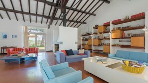 Un salon spacieux doté d’un haut plafond, de bibliothèques encastrées en bois et de différents types de sièges, notamment des canapés et une table basse.