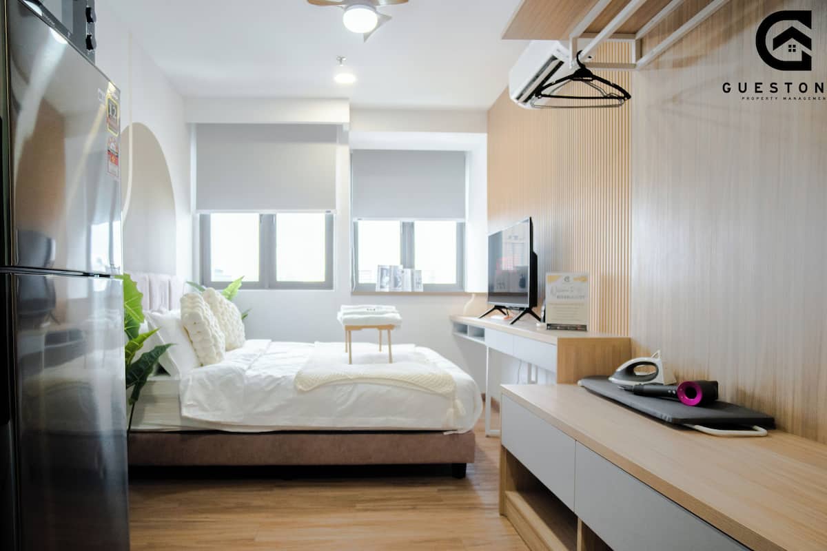 A modern hotel room with a bed, a desk, a TV, and a refrigerator.