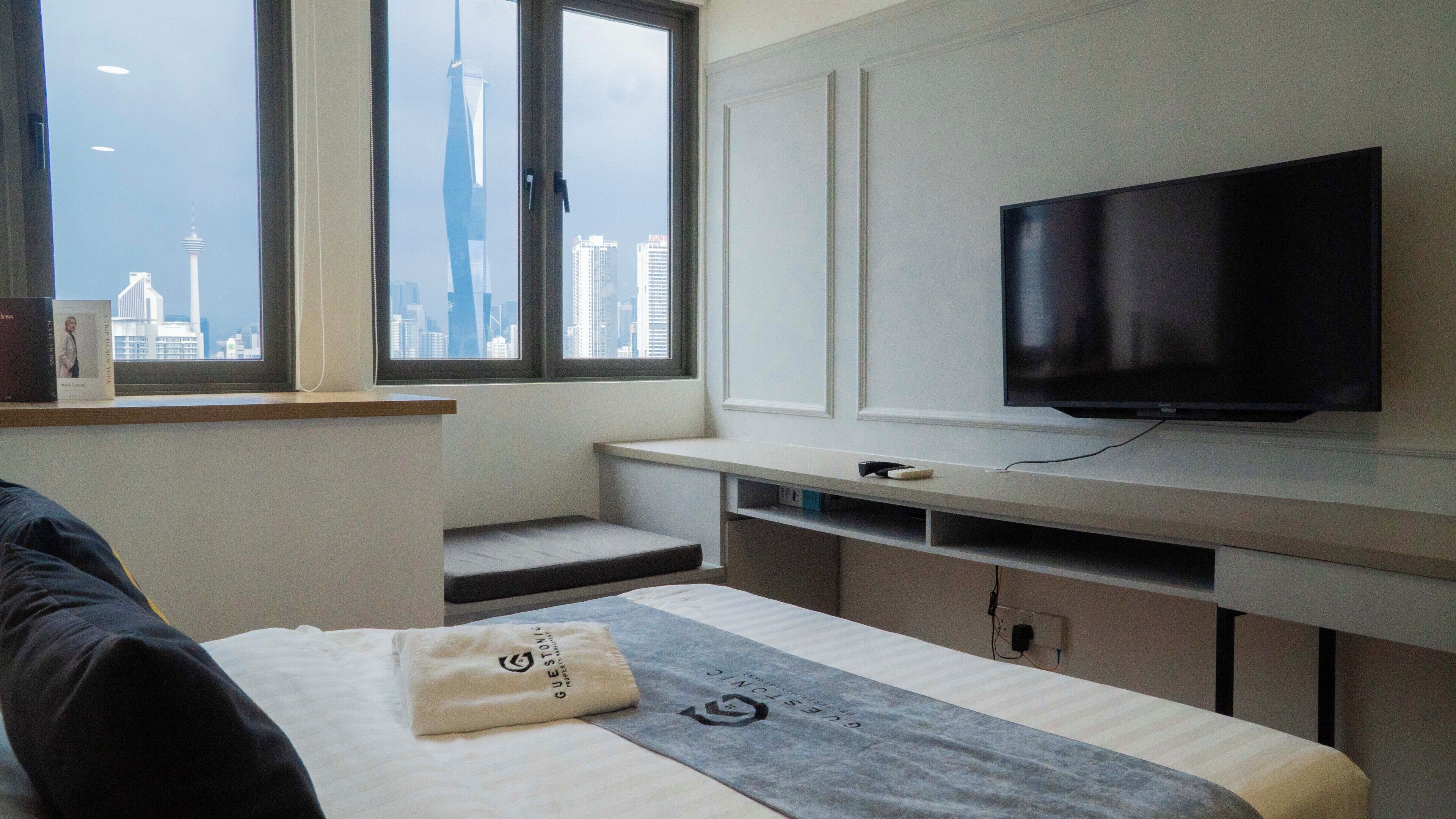 Une chambre d’hôtel avec un lit, une télévision, une fenêtre donnant sur la ville et un petit bureau.