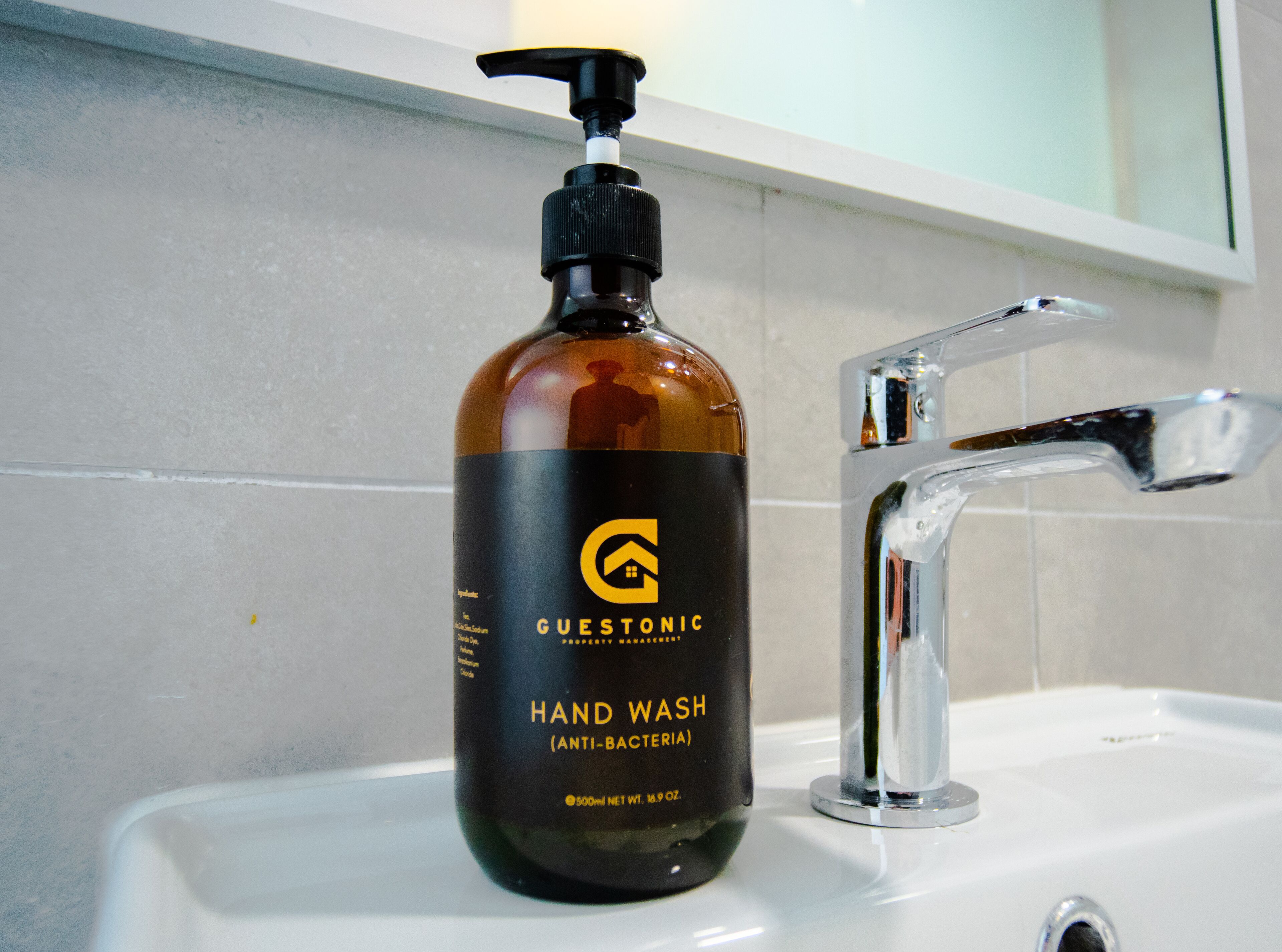 A hand wash bottle labeled 'Guestonic' next to a bathroom sink with a chrome faucet.