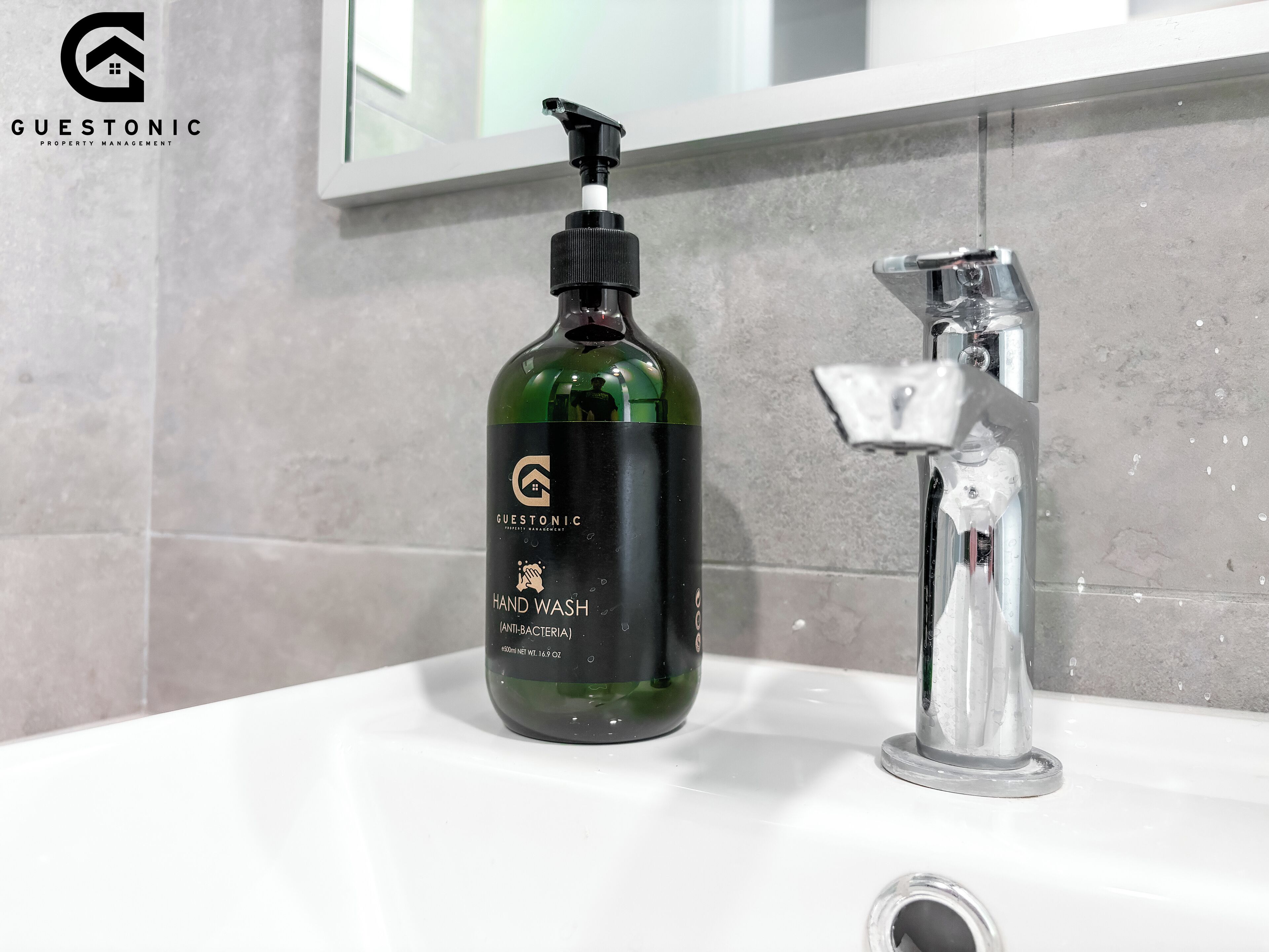 A bathroom with a green bottle of hand wash soap labeled 'GUESTONIC' and a modern faucet.