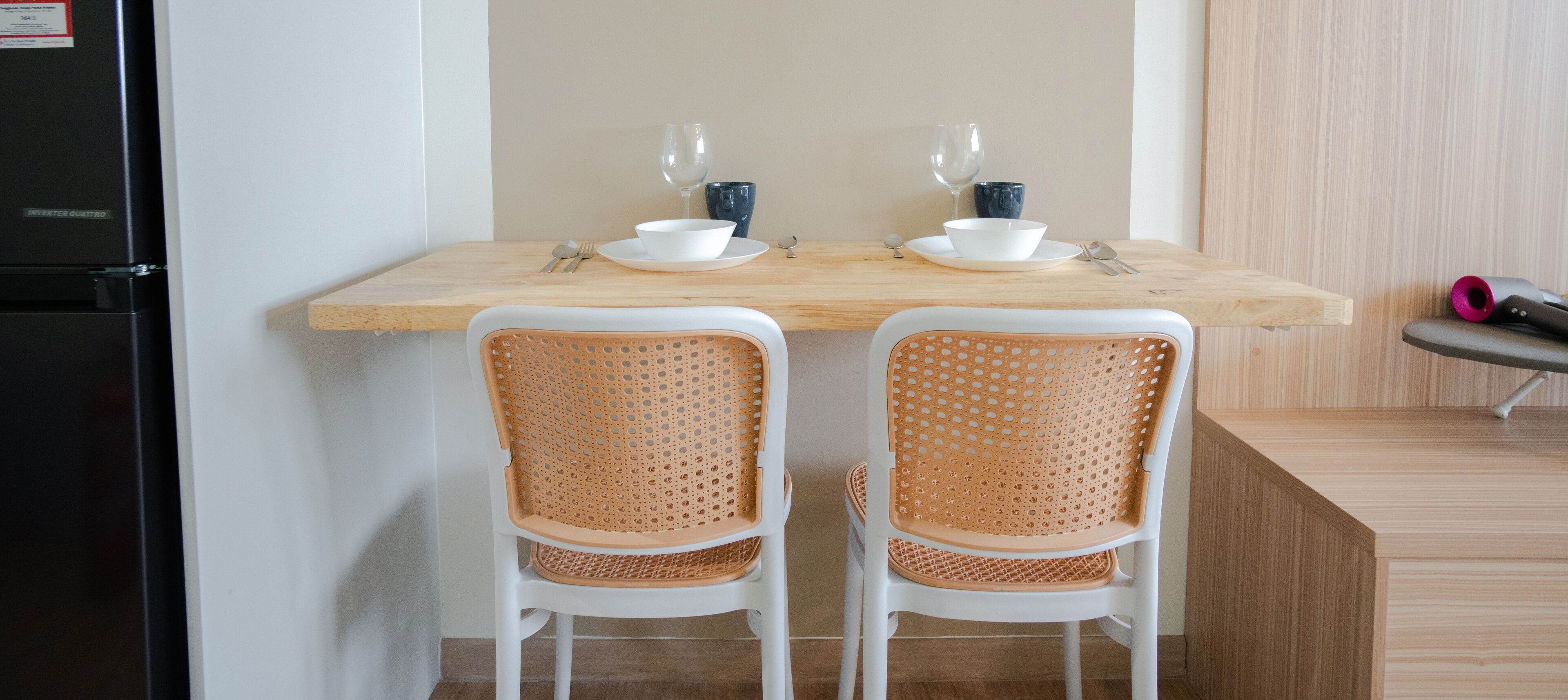 A kitchen with two white chairs, a wooden table, and a black refrigerator.