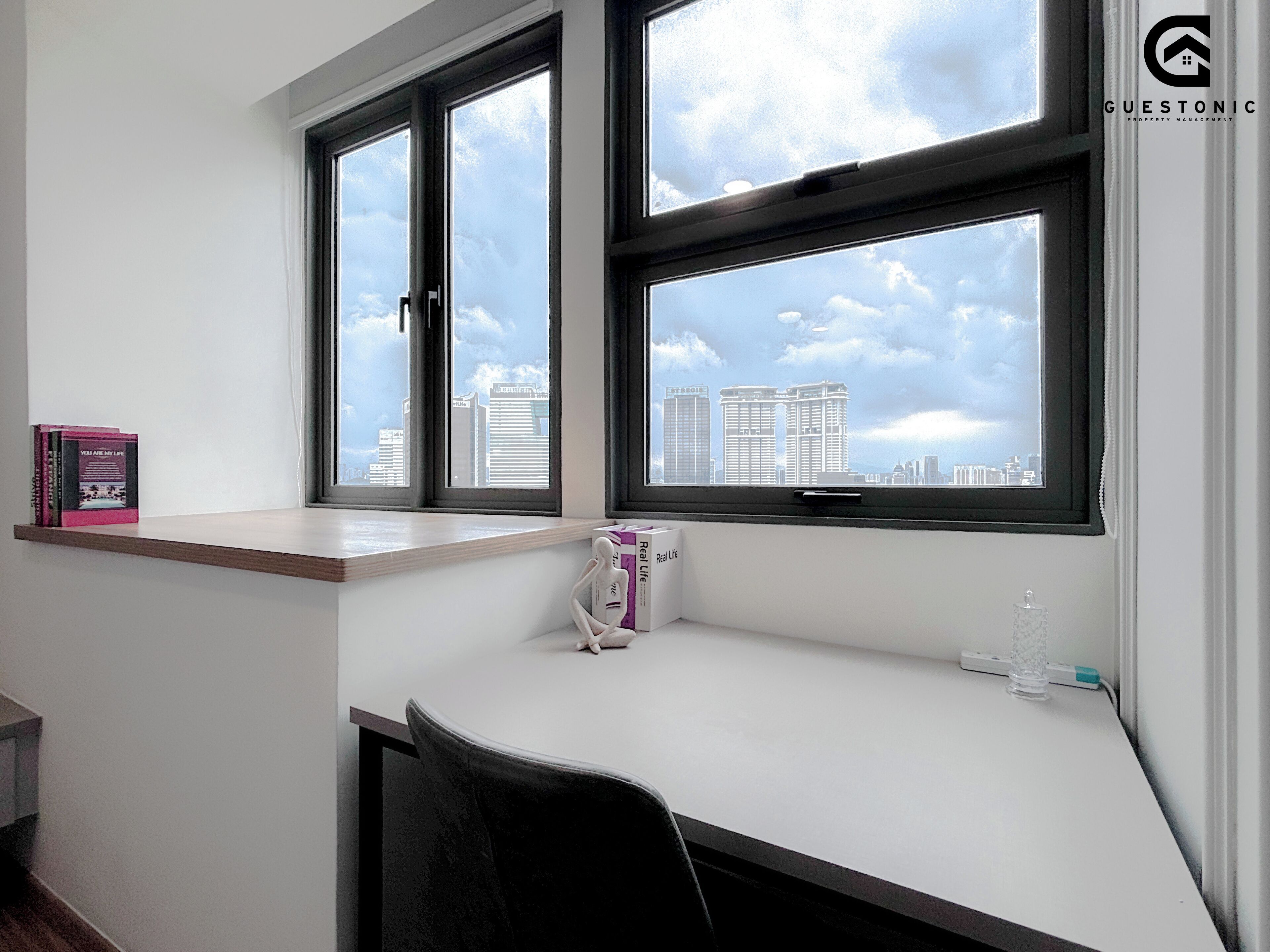 A modern office space with a desk, two windows, and a view of city buildings.