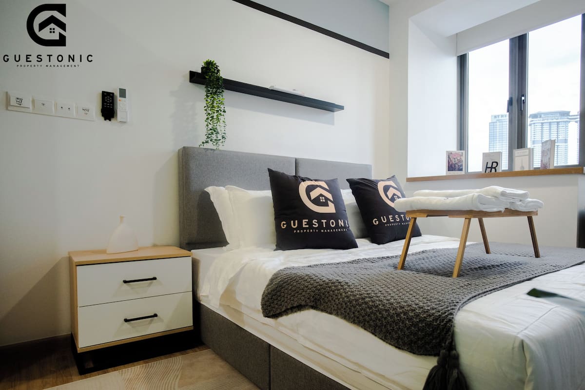 A modern bedroom with a bed, bedside tables, a nightstand, a window, and a view of the city.