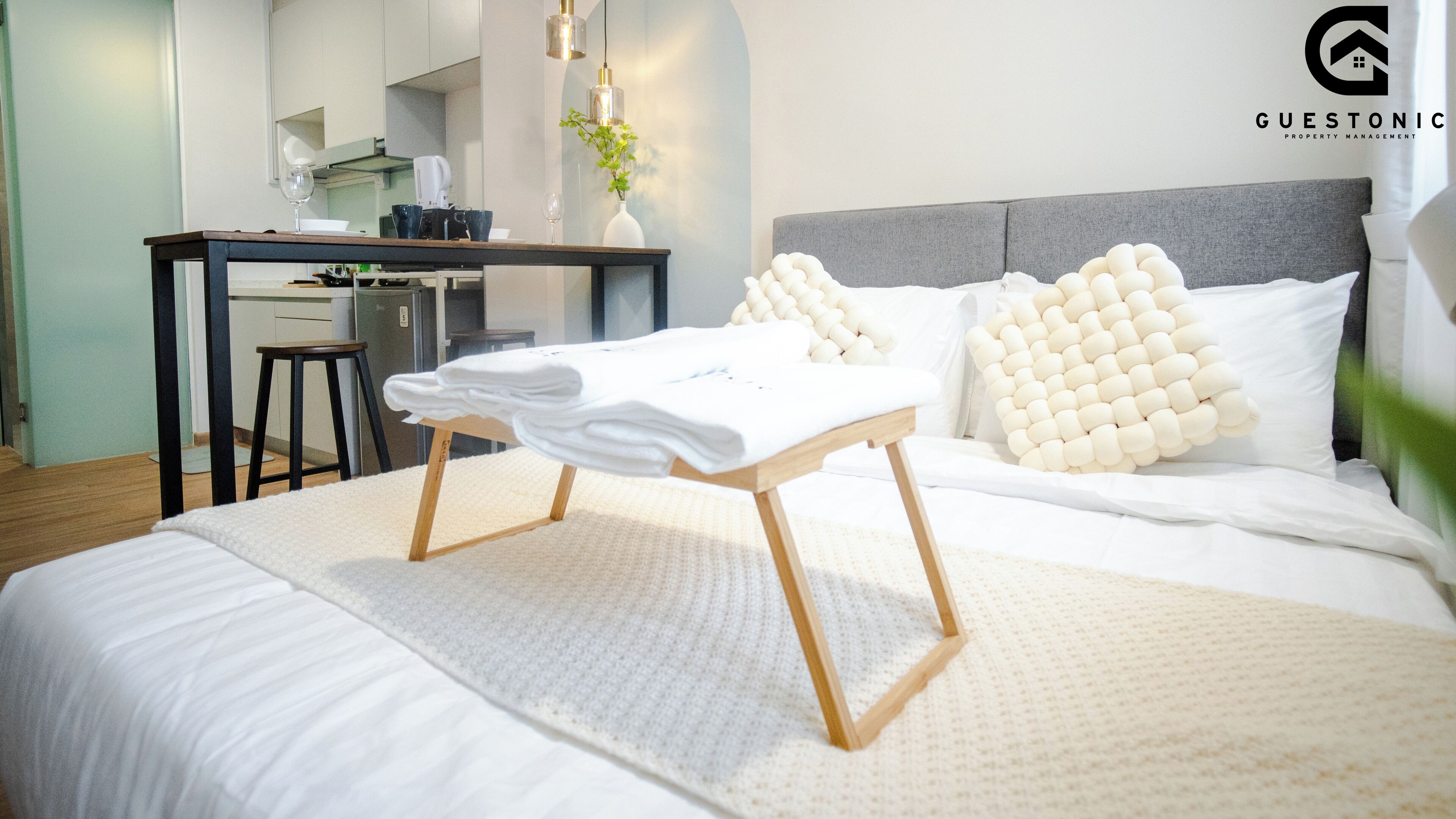 A modern hotel room with a neatly made bed, a small table with towels, a desk, and a chair.