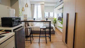 A compact kitchen with a microwave, a small refrigerator, and a dining area with stools. - Riveria City KL Sentral by Guestonic (Kuala Lumpur)