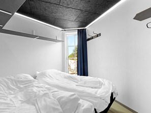 Un dormitorio moderno con cama, ventana con cortinas e iluminación empotrada en el techo.
