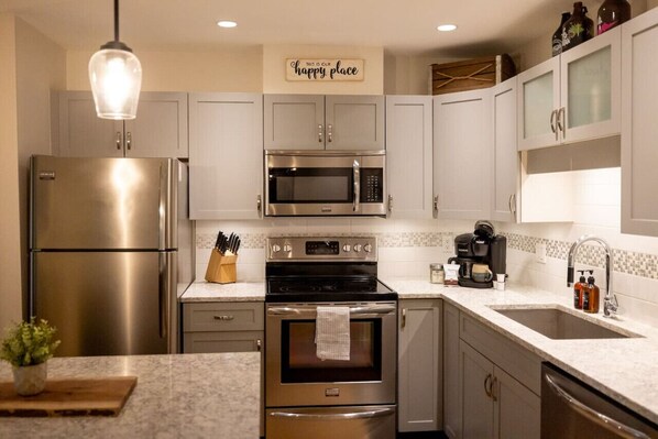A modern kitchen with stainless steel appliances, a marble countertop, and a 'happy place' sign.