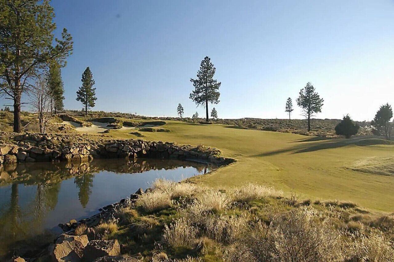 Ein Golfplatz mit Teich, Bäumen und blauem Himmel.