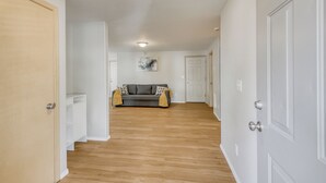 A hallway with wooden flooring, white walls, and a gray sofa with patterned cushions. - 3-bedroom house, good for families (Vancouver)
