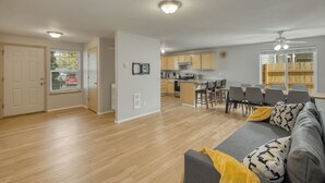 A spacious living room with a gray sofa, a dining area with a table and chairs, a kitchen with wooden cabinets, and a ceiling fan. - 3-bedroom house, good for families (Vancouver)