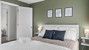A neatly made bed with white and beige bedding, a white headboard, and three framed floral wall art pieces.