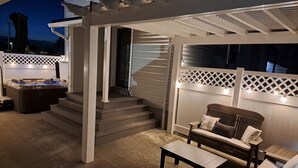 A covered outdoor seating area with a hot tub, a wooden bench, and a table.