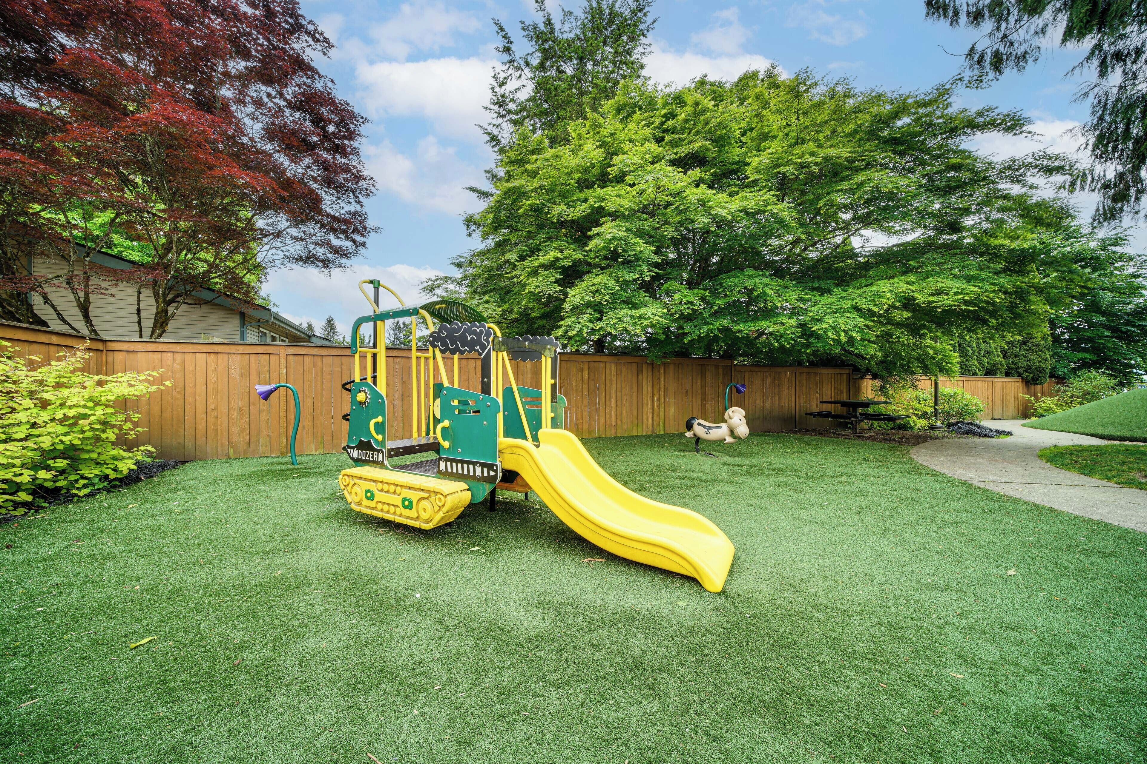 Ein Spielplatz mit Rutsche und Klettergerüst, umgeben von einem Holzzaun und Bäumen.