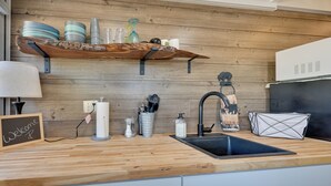 Een keuken met een houten aanrecht, een zwarte spoelbak en een plank erboven met borden en glazen.