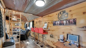 Interior rústico de una cabaña con detalles de madera, una litera, taburetes rojos, un cofre de madera con un letrero de bienvenida y una fotografía enmarcada de caballos.