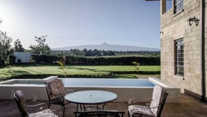 Un patio con una mesa redonda y cuatro sillas, una piscina y vistas a un paisaje verde con montañas al fondo.