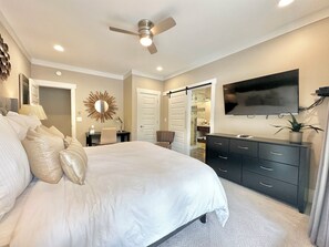 A bedroom with a large bed, a desk, a dresser, a ceiling fan, a TV, and a bathroom visible through an open door. - LOWER Level of "Your Big Lake House" - Firepit, Kayaks, HotTub, etc.  (Cedar Bluff)