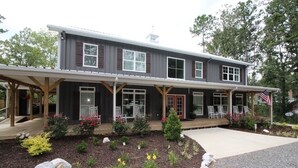 A two-story building with a covered porch, a front door, and a small garden area with plants and rocks. - LOWER Level of "Your Big Lake House" - Firepit, Kayaks, HotTub, etc.  (Cedar Bluff)