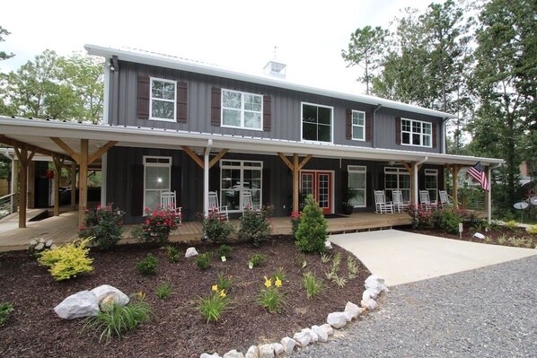 A two-story building with a covered porch, a front door, and a small garden area with plants and rocks. - LOWER Level of "Your Big Lake House" - Firepit, Kayaks, HotTub, etc.  (Cedar Bluff)