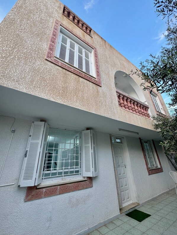 Un edificio a due piani con facciata strutturata, un balcone con ringhiera e una porta con una piccola finestra.
