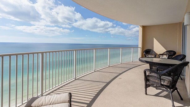 Een balkon met uitzicht op de oceaan, een ronde tafel met stoelen en een balustrade.