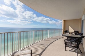 A balcony with a view of the ocean, a round table with chairs, and a railing.