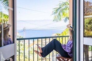 A person sitting on a balcony with a view of the ocean and palm trees. - Palm Tree House by Homie (São Vicente)