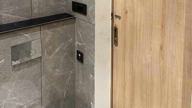 Une salle de bain avec un mur en marbre, une porte en bois et un plan de toilette noir.