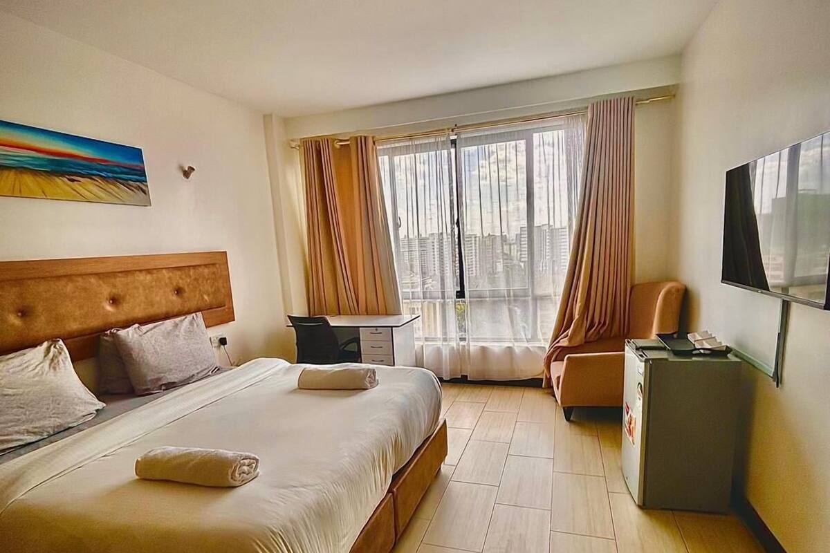 A hotel room with a large bed, a desk, a chair, a TV, and a window with curtains.