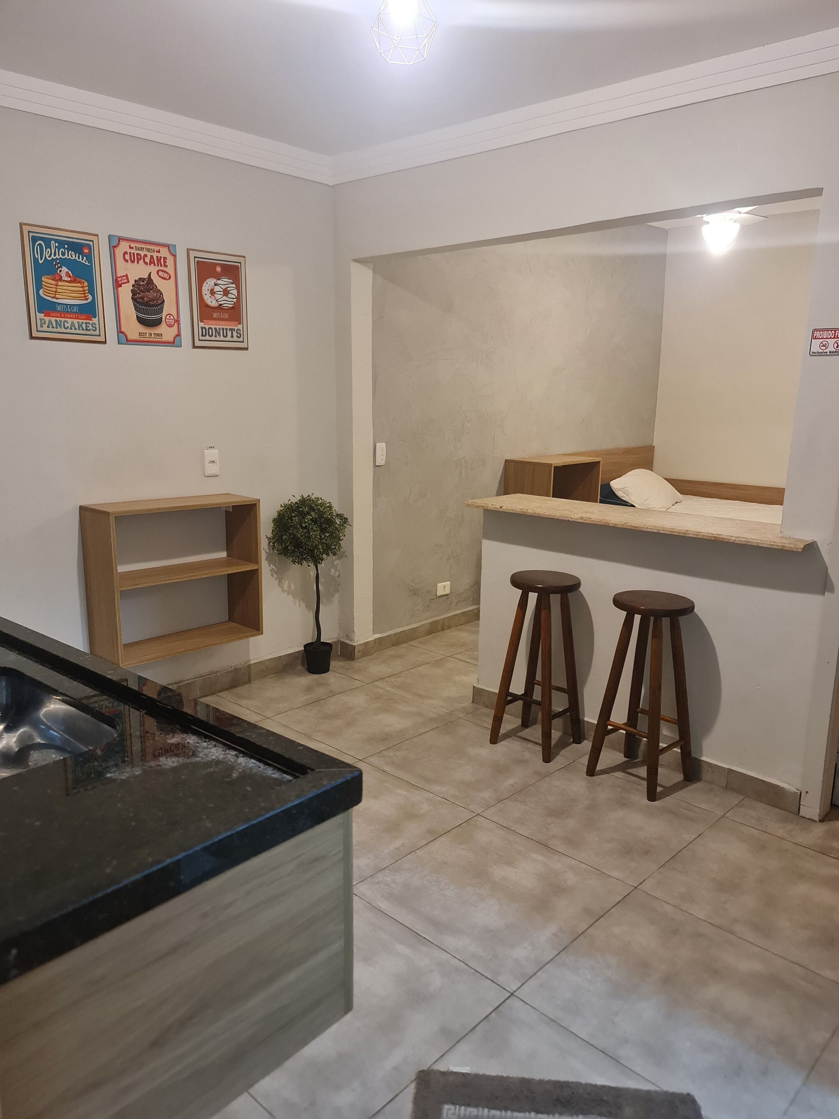 Una cocina compacta con encimera, un lavamanos, una planta pequeña y una zona de bar con taburetes.