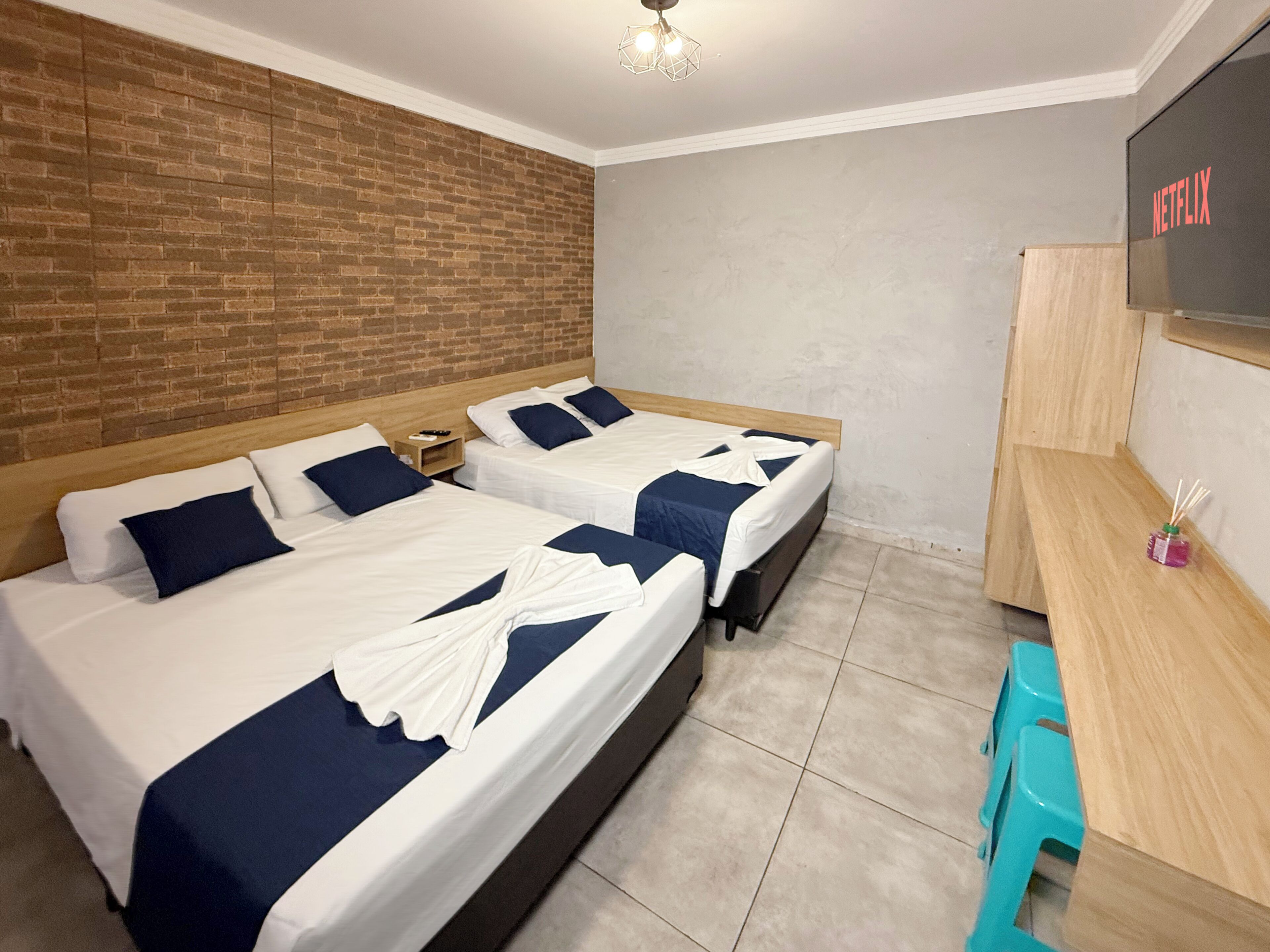 A hotel room with two beds, a wooden desk, a TV, and a brick wall.