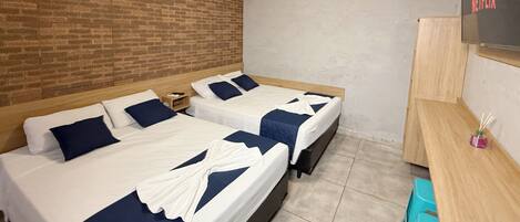 A hotel room with two beds, a wooden desk, a TV, and a brick wall.