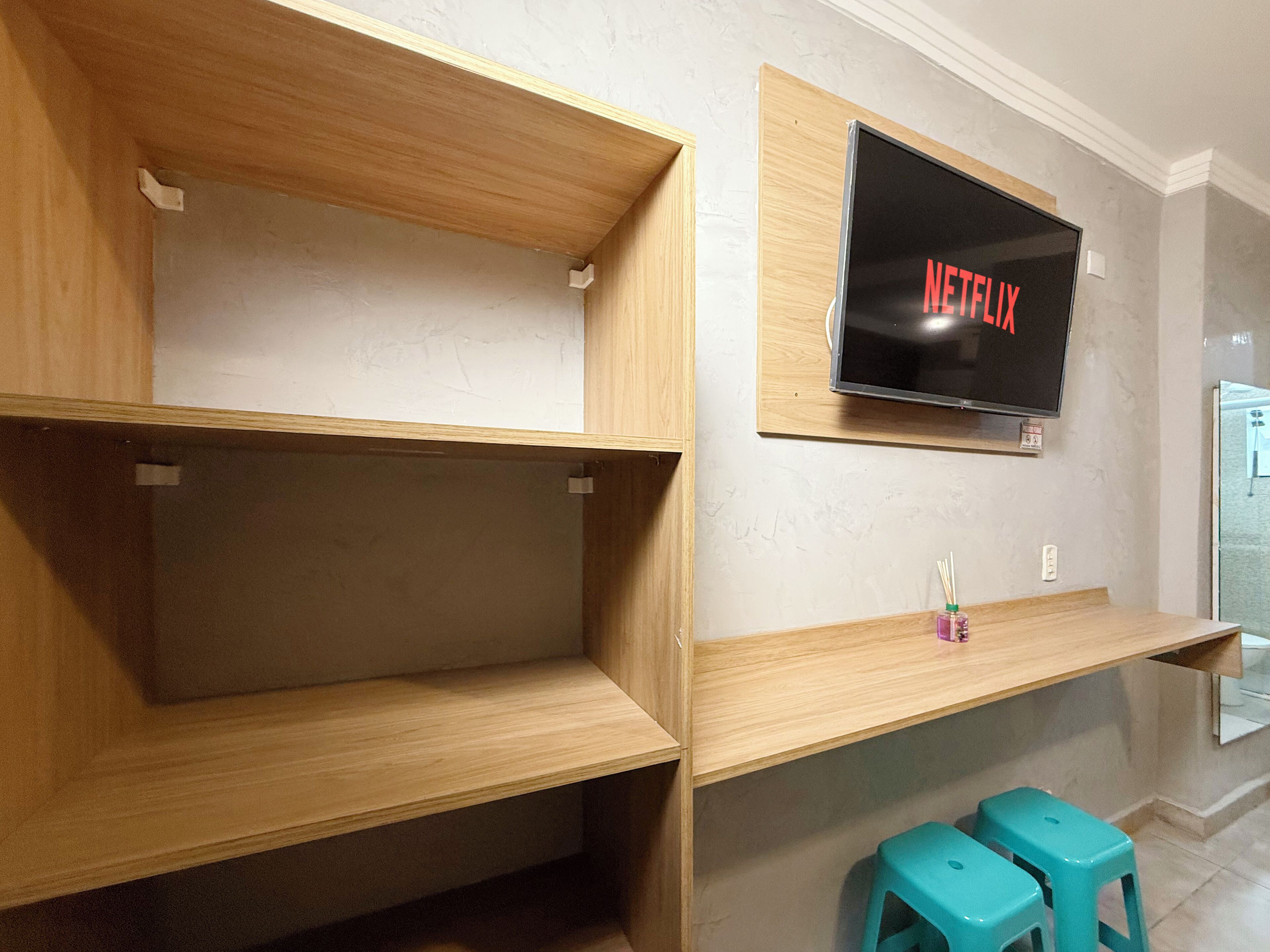 A room with wooden shelves, a mounted TV displaying 'NETFLIX', and two turquoise stools.