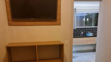 A bedroom with a bed, a wooden shelf unit, a television mounted on the wall, and a view of the outside through an open door.