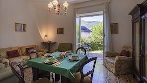 Ein Essbereich mit Tisch für vier Personen, Stühlen, einer Chandelier und Blick auf Grünfläche draußen.