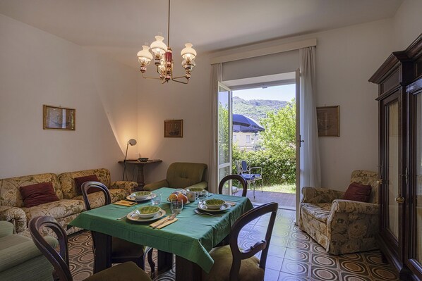 A dining area with a table set for four, chairs, a chandelier, and a view of greenery outside.