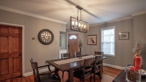 Un coin repas avec une table en bois, des chaises, un lustre et une horloge au mur.