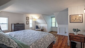 Une chambre à coucher comprenant un lit, une commode, une chaise, une lampe et un tableau accroché au mur.