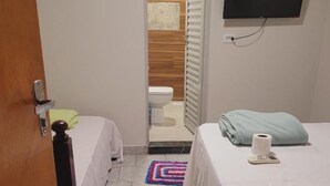Ein kleines, sauberes Zimmer mit zwei Betten, einer Toilette und einem Fernseher.