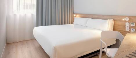 A modern hotel room with a large bed, a bedside table, a chair, and a control panel on the wall.