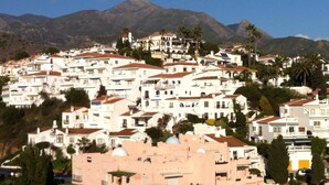 A hillside town with white buildings, some with domed roofs, and palm trees.