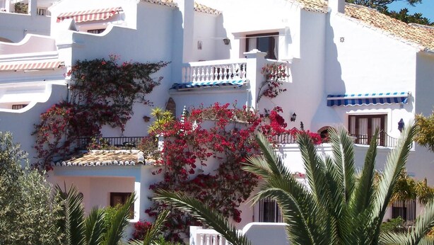 A white building with balconies, red flowers, and a tiled roof.