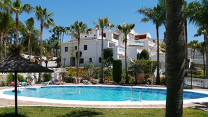 A swimming pool surrounded by palm trees and a white building with balconies.