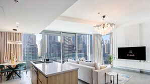 A modern living room with a large window, a sofa, a dining area, and a TV on the wall. - Deluxe 1BR Corner Suite with Marina Views (Dubai)