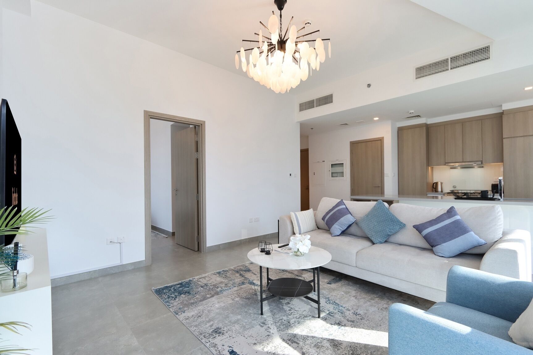 A modern living room with a white sofa, blue armchairs, a coffee table, and a chandelier.
